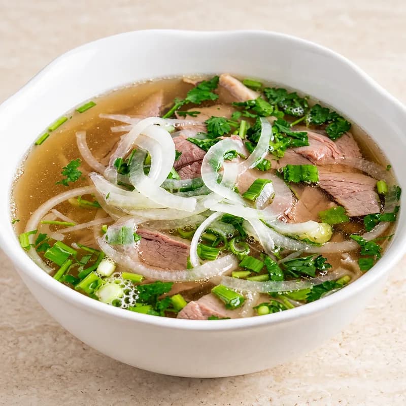 A bowl of steak and brisket phở with onion, green onion and rice noodles